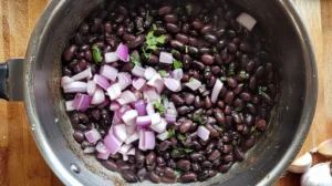 Black beans cooking in a pot with onions and garlic on the side.