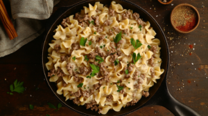 Ground beef and noodles casserole with golden cheese topping and fresh herbs in a rustic dish.