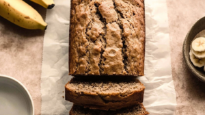 Banana bread no baking soda being sliced with a bread knife, revealing the soft and moist crumb, served on a rustic wooden cutting board.